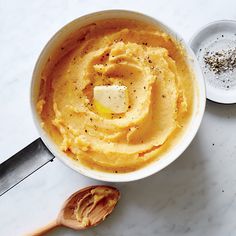 a white bowl filled with mashed potatoes next to a wooden spoon on a marble surface