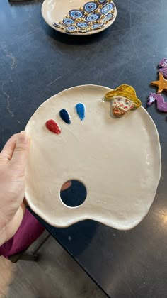 a person is holding a plate with paint on it and some other plates in the background