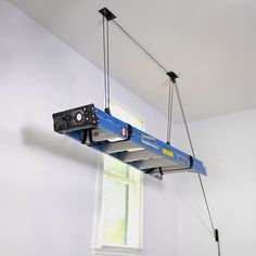 a blue crane is suspended from the ceiling by two wires, with a window in the background