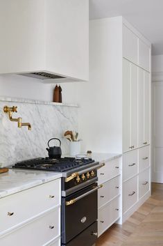 a stove top oven sitting inside of a kitchen next to white cupboards and drawers