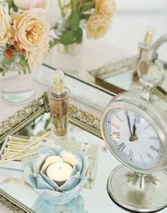 there is a small clock and some flowers on the table