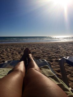 a person laying on top of a beach next to the ocean under a blue sky