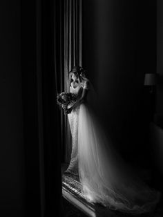 a woman standing in front of a window with her dress on and holding a bouquet