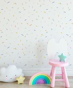 a white wall with sprinkles on it and a pink chair next to the rainbow