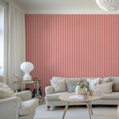 a living room with pink striped wallpaper and white couches in front of a coffee table