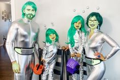 three people dressed in silver posing for a photo with one holding a purple purse and the other wearing green hair