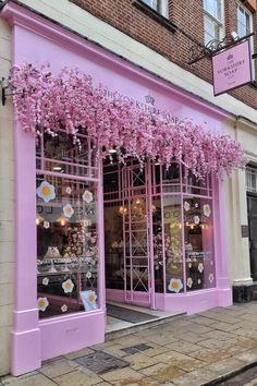 a storefront with pink flowers on the outside and purple windows in front, along side a brick building