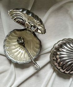 two silver dishes with spoons on a white cloth