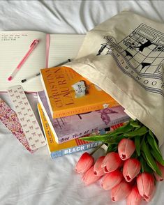 a bunch of books sitting on top of a bed next to tulips and a bag