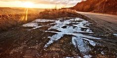 the sun is setting on an empty road with snow and grass all over it's surface