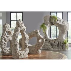 three sculptures sitting on top of a wooden table in front of large windows with plants growing out of them