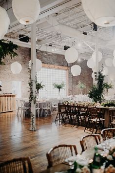 a room filled with lots of tables covered in white paper lanterns and hanging planters