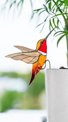 a glass hummingbird sitting on top of a white pot next to a green plant