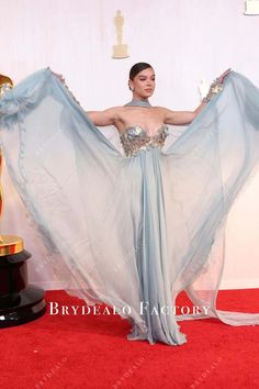 a woman in a blue dress holding an award on the red carpet with her hands behind her back