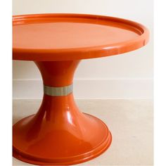 an orange table with silver trim around the top and bottom edge, sitting on a white tile floor