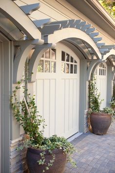 two large planters sitting next to each other on a brick walkway in front of a house