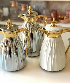 two silver and gold coffee pots on a counter top with other items in the background