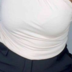 a woman wearing a white top and black pants with her hand on her hip while looking at the camera