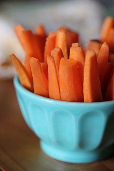 a blue bowl filled with sliced carrots on top of a wooden table