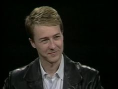 a man wearing a black leather jacket and white shirt is talking to someone in front of him