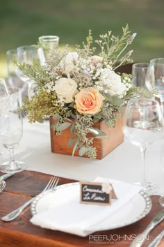 an arrangement of flowers and greenery in a wooden box on a table with place cards