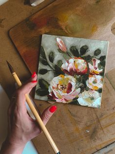 a woman's hand holding a paintbrush next to a painting on a canvas