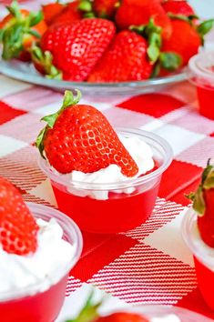 strawberries and whipped cream in plastic containers on a checkered tablecloth with plates full of strawberries