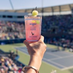 a person holding up a pink drink in front of a crowd at a tennis match