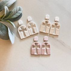 three pairs of pink and white earrings sitting on top of a table next to a plant