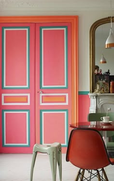 a dining room with chairs and a table in front of an orange door that is painted pink