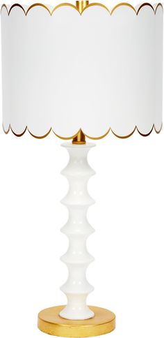 a white and gold lamp with a white shade on the top, sitting against a white background