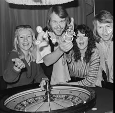 three women and one man are playing roulege at a casino table with their hands in the air