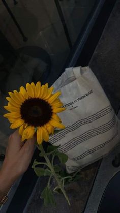 a person holding a sunflower in front of a white bag with writing on it