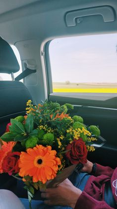 a woman sitting in the back seat of a car holding a bouquet of orange and yellow flowers