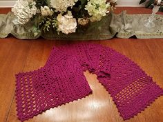 two crocheted shawls sitting on top of a wooden floor next to flowers