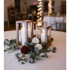 two candles are sitting on a table with flowers and greenery