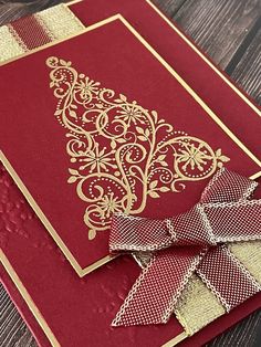 a red and gold christmas card with a bow on it's side, sitting on top of a wooden table