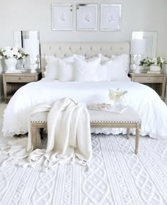 a bedroom with white bedding, pillows and blankets on the floor next to a bench