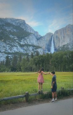 two children are standing in front of a large waterfall and mountains with their arms around each other