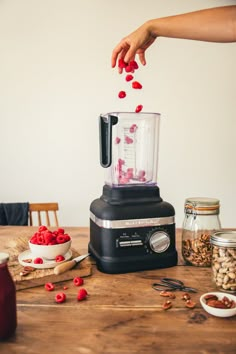 a person is adding raspberries to a blender on a table with other ingredients