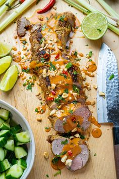 sliced up meat on a cutting board next to vegetables and a knife with lime wedges