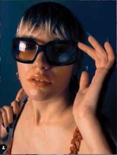 a woman wearing sunglasses and holding her hand up to the side with one eye open