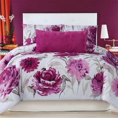 a bed with purple flowers on it and two lamps in the corner next to it