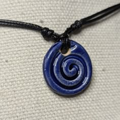 a blue necklace with a spiral design on it sitting on a white fabric surface,