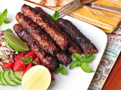 grilled meat and vegetables on a white plate with a fork, knife and napkin