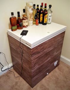 an electronic device sitting on top of a wooden cabinet with liquor bottles around it and cord plugged in