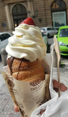 a person holding up a cupcake with whipped cream and a strawberries on top