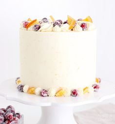 a white cake with cranberries and oranges on the top is sitting on a plate