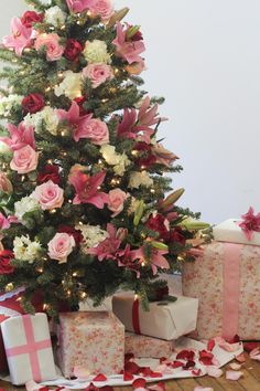 a small christmas tree with pink and white flowers next to wrapped presents on the floor