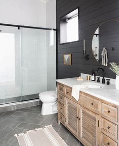 a white toilet sitting next to a walk in shower under a bathroom mirror on top of a wooden cabinet